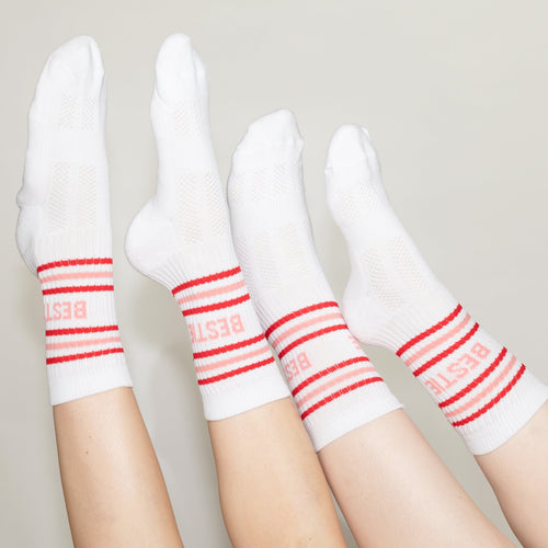 Four legs wearing white crew socks with red stripes and the word 'BESTIE' printed in red near the cuff, posed against a plain light beige background.